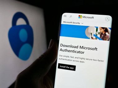 Stuttgart, Germany - 11-14-2023: Person holding cellphone with webpage of authentication app Microsoft Authenticator in front of business logo. Focus on center of phone display. clipart