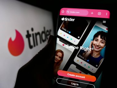 Stuttgart, Almanya - 11-14-2023: Şirket logosu önünde ABD online flört uygulaması Tinder 'ın web sayfası ile cep telefonu tutan kişi. Telefon ekranının merkezine odaklan.