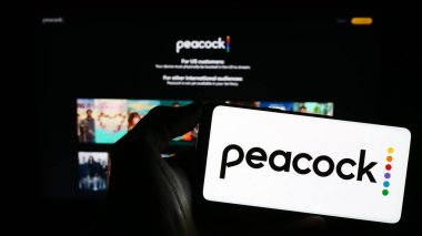 Stuttgart, Almanya - 11-14-2023: Amerikan video yayın servisi Peacock TV LLC 'nin logosu olan cep telefonu sahibi kişi web sayfasının önünde. Telefon ekranına odaklan.