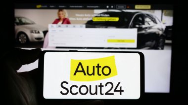 Stuttgart, Almanya - 11-14-2023: İnternet sayfası önünde Alman otomobil çevrimiçi pazar şirketi AutoScout24 GmbH logosuna sahip cep telefonu sahibi kişi. Telefon ekranına odaklan.