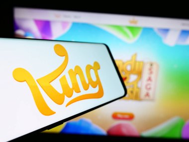 Stuttgart, Germany - 11-14-2023: Smartphone with logo of Swedish video game development company King.com Limited in front of website. Focus on center-left of phone display. clipart