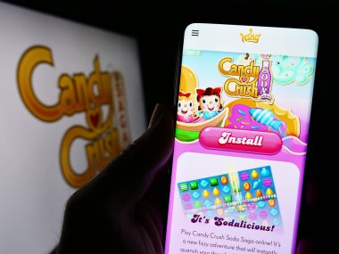 Stuttgart, Almanya - 11-14-2023: Fayansla eşleşen video oyunu Candy Crush Saga 'nın web sayfası ile logo önünde cep telefonu tutan kişi. Telefon ekranının merkezine odaklan.
