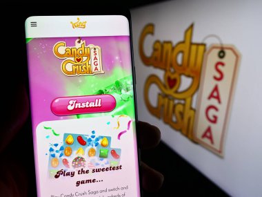 Stuttgart, Almanya - 11-14-2023: Kiremit eşleşen video oyunu Candy Crush Saga 'nın web sayfası olan cep telefonunu logonun önünde tutan kişi. Telefon ekranının merkezine odaklan.