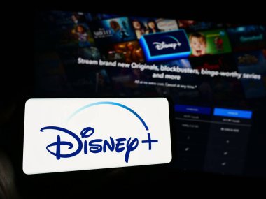 Stuttgart, Almanya - 11-14-2023: Web sayfasının önünde Amerikan video-talep yayın servisi Disney Plus 'ın logosu olan cep telefonu sahibi kişi. Telefon ekranına odaklan.