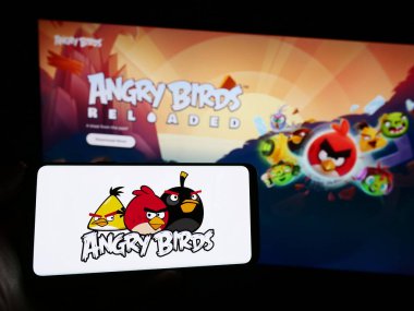 Stuttgart, Germany - 11-14-2023: Person holding mobile phone with logo of artillery video game Angry Birds in front of company web page. Focus on phone display. clipart