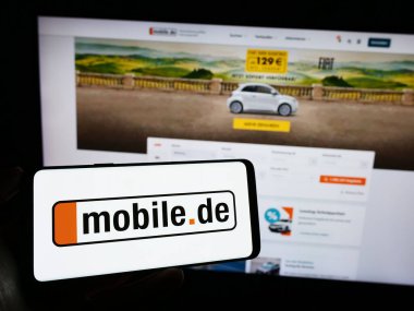 Stuttgart, Almanya - 11-14-2023: İnternet sayfasının önünde Alman otomobil çevrimiçi pazar şirketi mobile.de GmbH 'nin logosuna sahip cep telefonu sahibi kişi. Telefon ekranına odaklan.