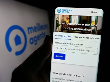 Stuttgart, Almanya - 11-15-2023: Fransız emlak platformu şirketi MeilleursAgents 'in logo önündeki web sayfası ile cep telefonu tutan kişi. Telefon ekranının merkezine odaklan.