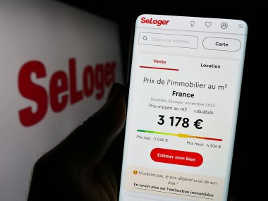 Stuttgart, Almanya - 11-15-2023: Fransız emlak platformu şirketi SeLoger 'ın logosu önünde web sayfası ile akıllı telefon tutan kişi. Telefon ekranının merkezine odaklan.