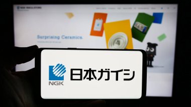 Stuttgart, Almanya - 11-15-2023: Japon seramik şirketi NGK Insulators Ltd. nin logosuna sahip akıllı telefon sahibi kişi web sitesinin önünde. Telefon ekranına odaklan.