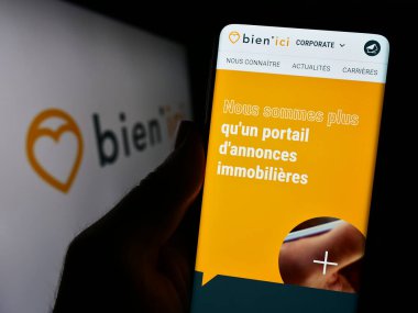 Stuttgart, Almanya - 11-15-2023: Fransız emlak araştırma şirketi Bien 'ici SAS' ın web sayfası ile logo önünde cep telefonu tutan kişi. Telefon ekranının merkezine odaklan.