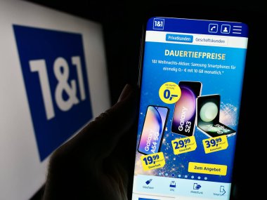 Stuttgart, Almanya - 11-15-2023: Alman firması 1und1 Telekomünikasyon SE 'nin web sayfası ile iş logosu önünde cep telefonu tutan kişi. Telefon ekranının merkezine odaklan.