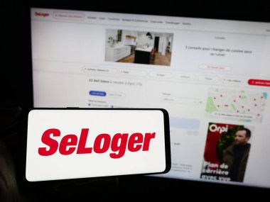 Stuttgart, Almanya - 11-15-2023: Fransız emlak platformu şirketi SeLoger 'ın logosuna sahip cep telefonu sahibi kişi iş sayfasının önünde. Telefon ekranına odaklan.