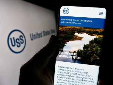 Stuttgart, Almanya - 09-25-2023: Birleşik Devletler Çelik Şirketi 'nin (US Steel) logosu önünde cep telefonu bulunduran kişi. Telefon ekranının merkezine odaklan.
