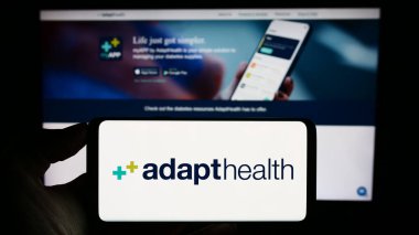 Stuttgart, Almanya - 09-25-2023: ABD 'li sağlık şirketi AdaptHealth LLC' nin logosuna sahip cep telefonu sahibi kişi iş sayfası önünde. Telefon ekranına odaklan.