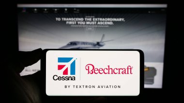 Stuttgart, Almanya - 09-25-2023: ABD 'li havacılık şirketi Textron Aviation Inc.' in logosuyla cep telefonu tutan kişi iş sayfasının önünde. Telefon ekranına odaklan.