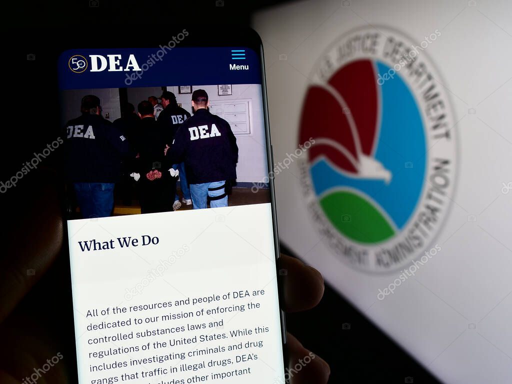 Stuttgart, Germany - 11-11-2023: Person holding cellphone with webpage of United States Drug Enforcement Administration (DEA) in front of seal. Focus on center of phone display.