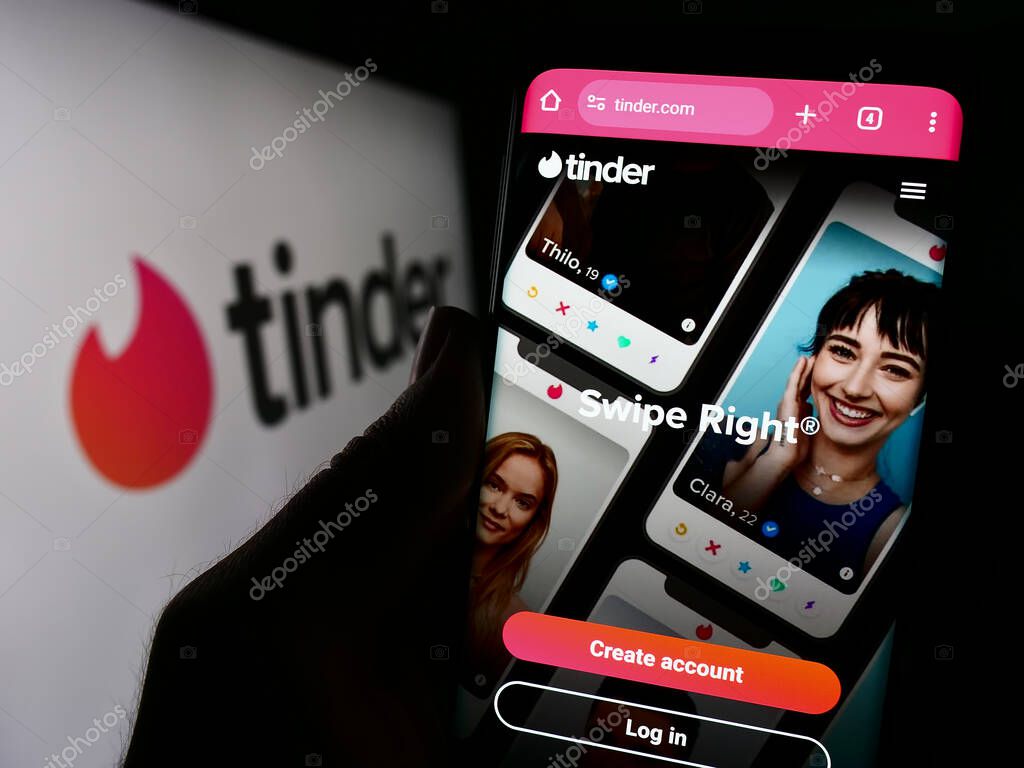 Stuttgart, Germany - 11-14-2023: Person holding cellphone with webpage of US online dating app Tinder in front of company logo. Focus on center of phone display.