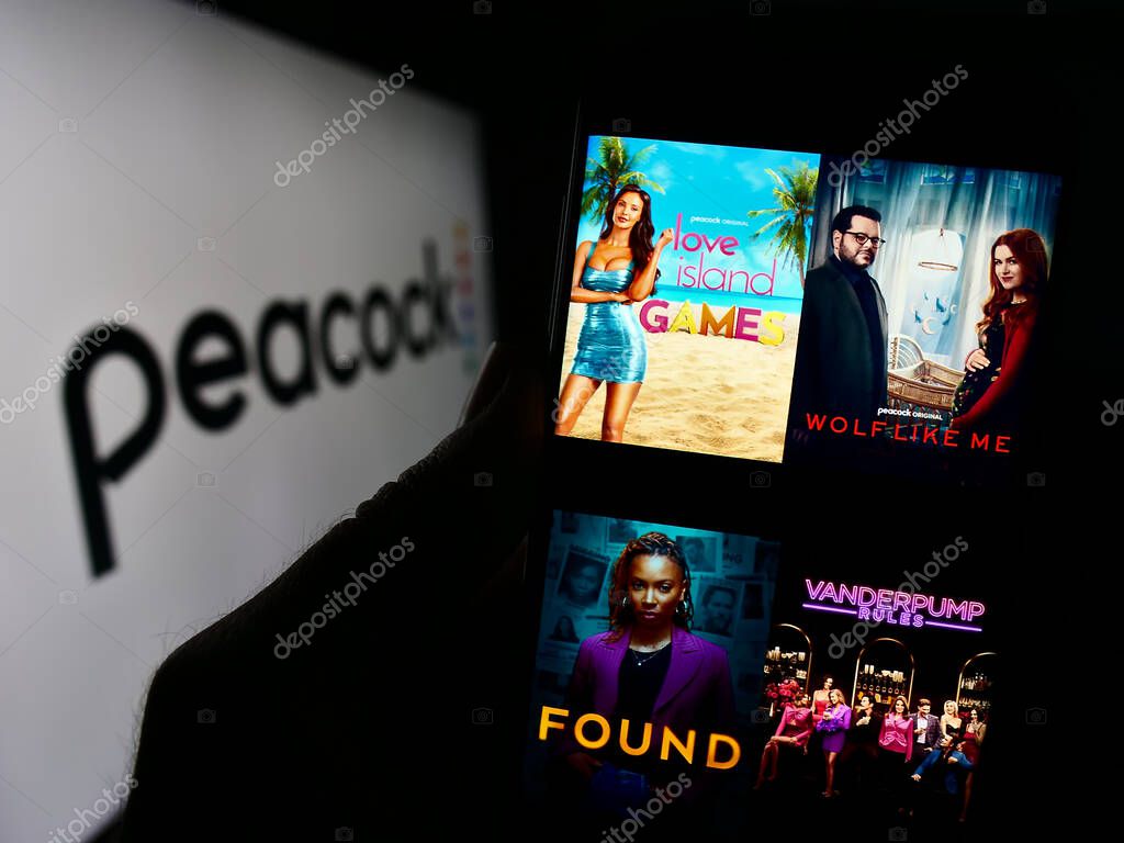 Stuttgart, Germany - 11-14-2023: Person holding cellphone with webpage of US video streaming service company Peacock TV LLC in front of logo. Focus on center of phone display.