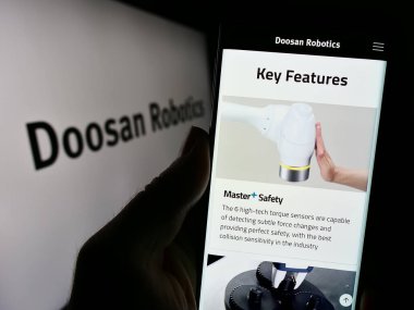 Stuttgart, Almanya - 09-28-2023: Koreli robot şirketi Doosan Robotics Inc. 'in internet sitesi ile iş logosu önünde cep telefonu tutan kişi. Telefon ekranının merkezine odaklan.