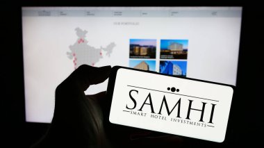 Stuttgart, Almanya - 09-28-2023: Hintli otel geliştirme şirketi Samhi Hotels Ltd. 'nin logosuyla cep telefonu tutan kişi iş sayfasının önünde. Telefon ekranına odaklan.