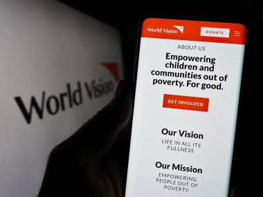 Stuttgart, Almanya - 10-06-2023: Dünya Vizyon Örgütü 'nün internet sayfası ile logo önünde akıllı telefon tutan kişi. Telefon ekranının merkezine odaklan.
