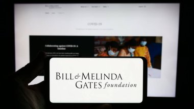 Stuttgart, Germany - 10-06-2023: Person holding smartphone with logo of American Bill and Melinda Gates Foundation (BMGF) in front of website. Focus on phone display. clipart