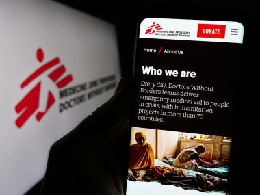 Stuttgart, Almanya - 10-06-2023: Sınırsız Doktorlar adlı yardım kuruluşunun logosu önündeki web sayfası ile akıllı telefon tutan kişi. Telefon ekranının merkezine odaklan.