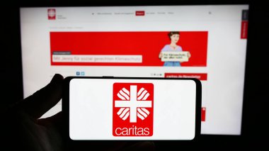 Stuttgart, Almanya - 10-08-2023: Alman örgütü Deutscher Caritasverband E.V. logosu olan akıllı telefon sahibi kişi İnternet sitesinin önünde. Telefon ekranına odaklan.