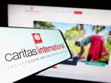 Stuttgart, Almanya - 10-08-2023: Yardım kuruluşu Caritas International 'ın logosuna sahip cep telefonu web sitesinin önünde. Telefon ekranının merkezine odaklan.