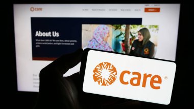 Stuttgart, Almanya - 10-08-2023: İnternet sitesi önünde üzerinde insani yardım kuruluşu CARE International 'ın logosu bulunan akıllı telefon sahibi kişi. Telefon ekranına odaklan.