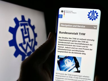 Stuttgart, Almanya - 10-08-2023: Logo önünde Bundesanstalt Technisches Hilfswerk (THW) organizasyonu web sitesi ile cep telefonu tutan kişi. Telefon ekranının merkezine odaklan.
