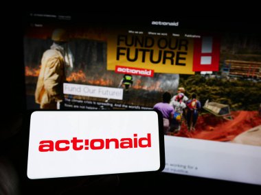 Stuttgart, Germany - 10-08-2023: Person holding cellphone with logo of international charity organization ActionAid in front of webpage. Focus on phone display. clipart