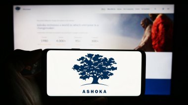 Stuttgart, Germany - 10-09-2023: Person holding cellphone with logo of social entrepreneurship organization Ashoka in front of webpage. Focus on phone display. clipart