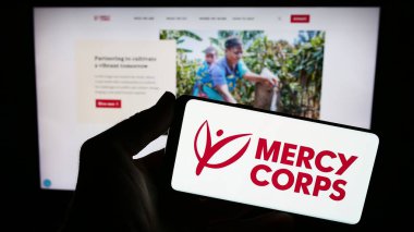 Stuttgart, Almanya - 10-09-2023: ABD 'li insani yardım kuruluşu Mercy Corps' un logosunu elinde tutan kişi web sitesi önünde. Telefon ekranına odaklan.