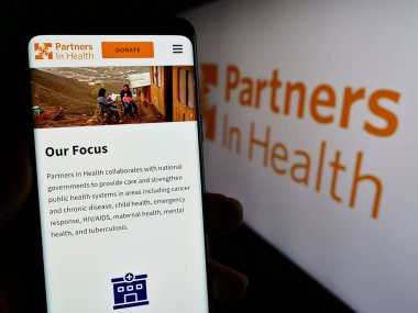 Stuttgart, Almanya - 10-10-2023: ABD 'li organizasyon Partners in Health (PIH) web sitesinin logo önünde akıllı telefon sahibi kişi. Telefon ekranının merkezine odaklan.