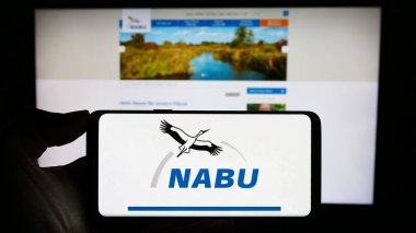 Stuttgart, Almanya - 10-10-2023: İşbirliği logosu Naturschutzbund Deutschland ile cep telefonu tutan kişi. (NABU) Web sayfasının önünde. Telefon ekranına odaklan.