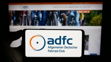 Stuttgart, Germany - 10-10-2023: Person holding cellphone with logo of Allgemeiner Deutscher Fahrrad-Club e.V. (ADFC) in front of webpage. Focus on phone display. clipart