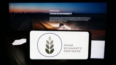 Stuttgart, Almanya - 10-11-2023: ABD 'li yatırım şirketi Paine Schwartz Partners LLLC' nin logosuyla cep telefonu tutan kişi iş sayfasının önünde. Telefon ekranına odaklan.