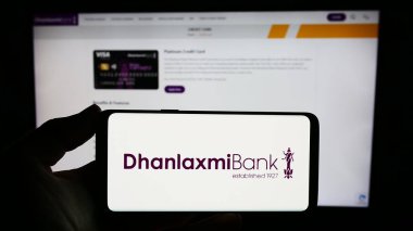 Stuttgart, Germany - 10-11-2023: Person holding smartphone with logo of Indian financial company Dhanlaxmi Bank Ltd. in front of website. Focus on phone display. clipart