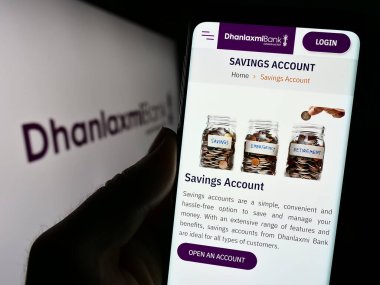 Stuttgart, Almanya - 10-11-2023: Hintli finans şirketi Dhanlaxmi Bank Ltd. 'nin internet sitesi ile logo önünde cep telefonu tutan kişi. Telefon ekranının merkezine odaklan.