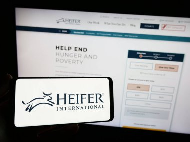 Stuttgart, Almanya - 10-11-2023: Gelişim organizasyonu Heifer International 'ın logosuna sahip akıllı telefonu web sitesi önünde tutan kişi. Telefon ekranına odaklan.