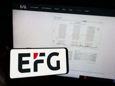 Stuttgart, Almanya - 10-13-2023: İsviçreli özel banka şirketi EFG International AG 'nin logosuna sahip cep telefonu sahibi kişi iş sayfasının önünde. Telefon ekranına odaklan.