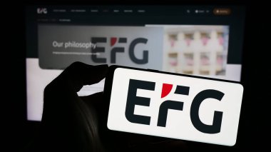 Stuttgart, Almanya - 10-13-2023: İsviçreli özel banka şirketi EFG International AG 'nin logosuna sahip akıllı telefon sahibi kişi web sitesinin önünde. Telefon ekranına odaklan.
