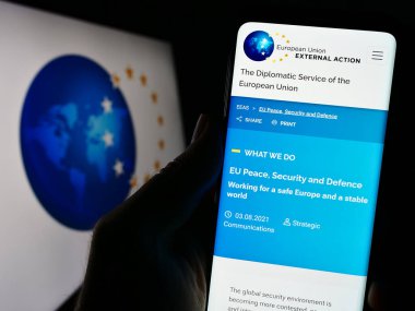 Stuttgart, Almanya - 10-16-2023: Logolu AB kurumu Avrupa Dış Eylem Servisi (AEAS) web sitesi ile cep telefonu bulunduran kişi. Telefon ekranının merkezine odaklan.