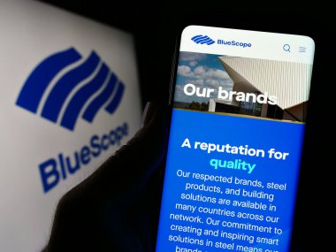 Stuttgart, Germany - 10-16-2023: Person holding cellphone with webpage of Australian company BlueScope Steel Limited in front of logo. Focus on center of phone display. clipart