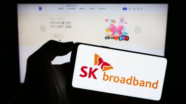 Stuttgart, Almanya - 10-16-2023: Koreli telekomünikasyon şirketi SK Broadband Inc. 'in logosuna sahip cep telefonu sahibi kişi web sayfasının önünde. Telefon ekranına odaklan.