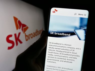 Stuttgart, Almanya - 10-16-2023: Koreli telekomünikasyon şirketi SK Broadband Inc. 'in internet sayfası ile logo önünde cep telefonu tutan kişi. Telefon ekranının merkezine odaklan.