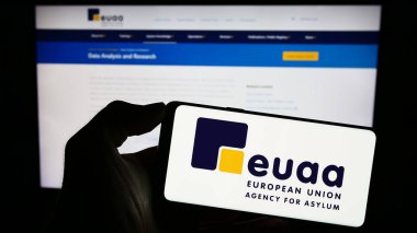 Stuttgart, Almanya - 10-17-2023: İnternet sayfası önünde Avrupa Birliği Sığınma Dairesi (EUAA) logosu bulunan kişi. Telefon ekranına odaklan.