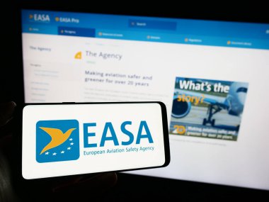 Stuttgart, Almanya - 10-17-2023: İnternet sayfasının önünde Avrupa Birliği Havacılık Güvenliği Ajansı (EASA) logosu bulunan cep telefonu sahibi kişi. Telefon ekranına odaklan.