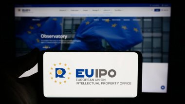 Stuttgart, Almanya - 10-17-2023: İnternet sitesi önünde üzerinde Avrupa Birliği Fikir Eserleri Ofisi (EUIPO) logosu bulunan kişi. Telefon ekranına odaklan.